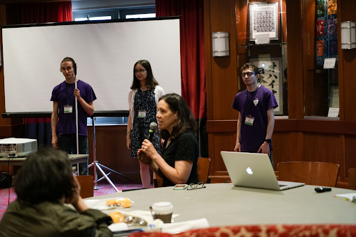 Kate Meredith (seated and speaking into a microphone) and three GLAS Education Interns (standing in front of a projection screen) present at the SciAccess 2019 Conference. Credit - SciAccess